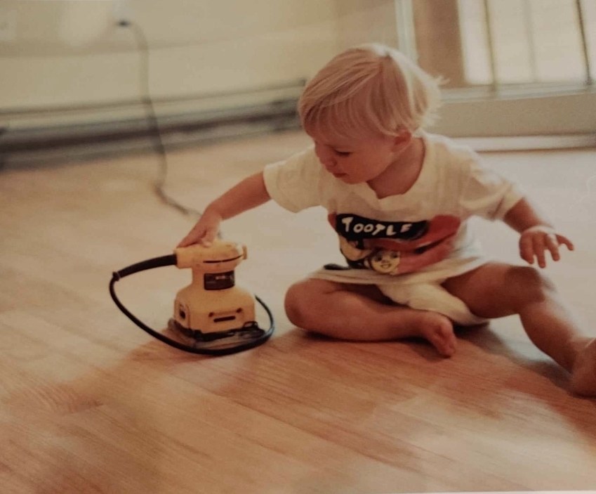 Christopher Aversa at age three running an orbital sander across a hardwood floor
